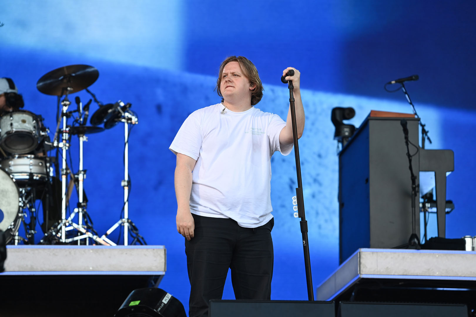 Lewis Capaldi is standing on stage holding a microphone.