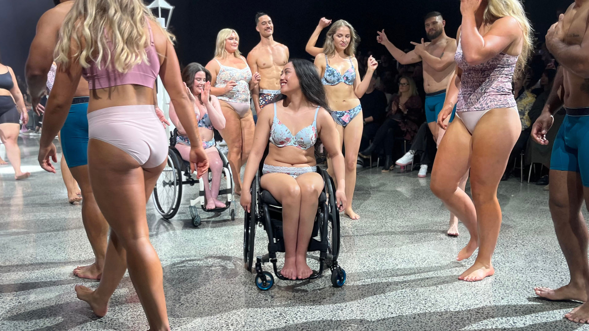 Chelsea is in her Jockey underwear and smiling. She is surrounded by other models on the runway.