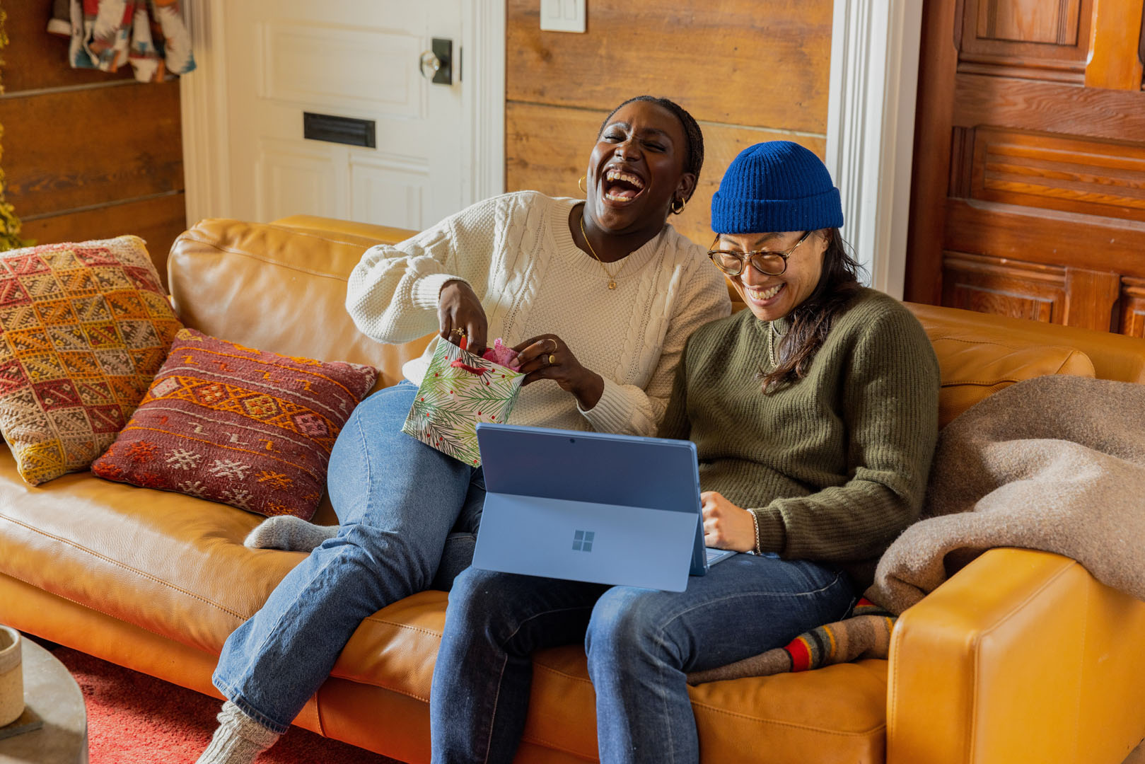 A stock image, featuring two people sitting on a couch, laughing. They have a tablet on their knee. 
