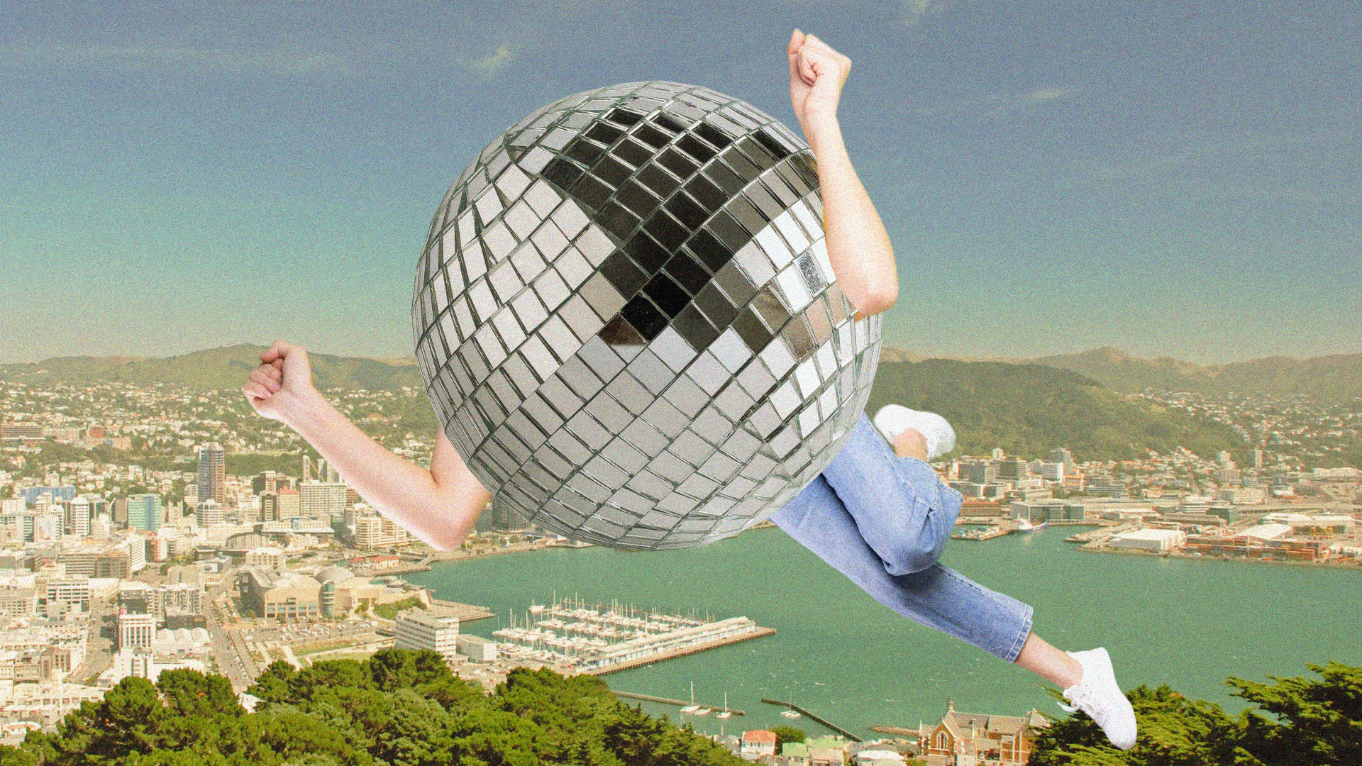 A person with a disco ball for a body flies through the air excitedly over a landscape of the Wellington Harbour.