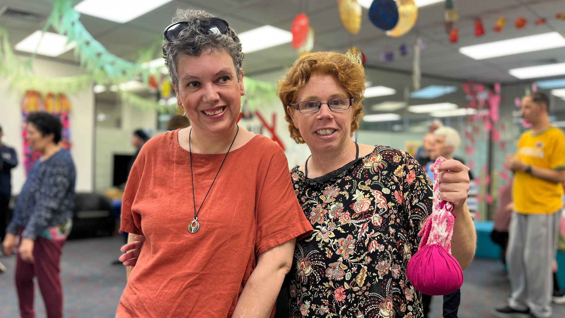 Tammy Pringle (left) and Teresa Nicol are performing at Te Hoenga Waka Kapa Haka Festival next week. Tammy wears a red t-shirt, and Teresa wears a black, floral top and holds a pink poi; they are both smiling.