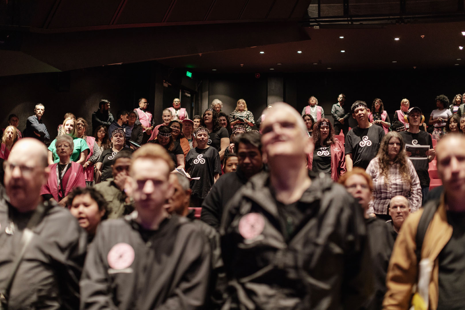 A large audience in a darkly-lit theatre watch performers at Te Hoenga Waka Kapa Haka Festival.