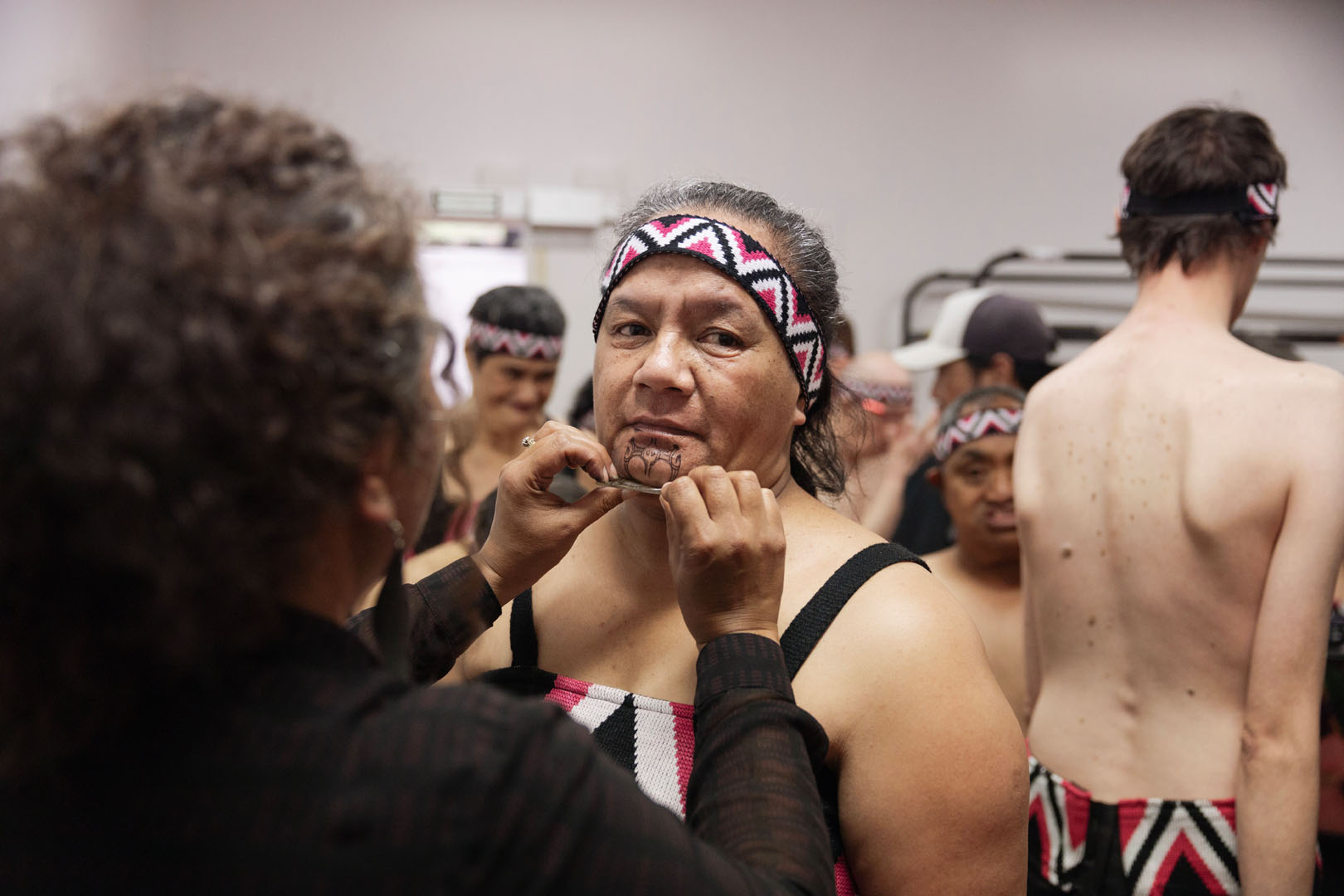 A kaihaka is having a stick-on ta moko applied to her chin.