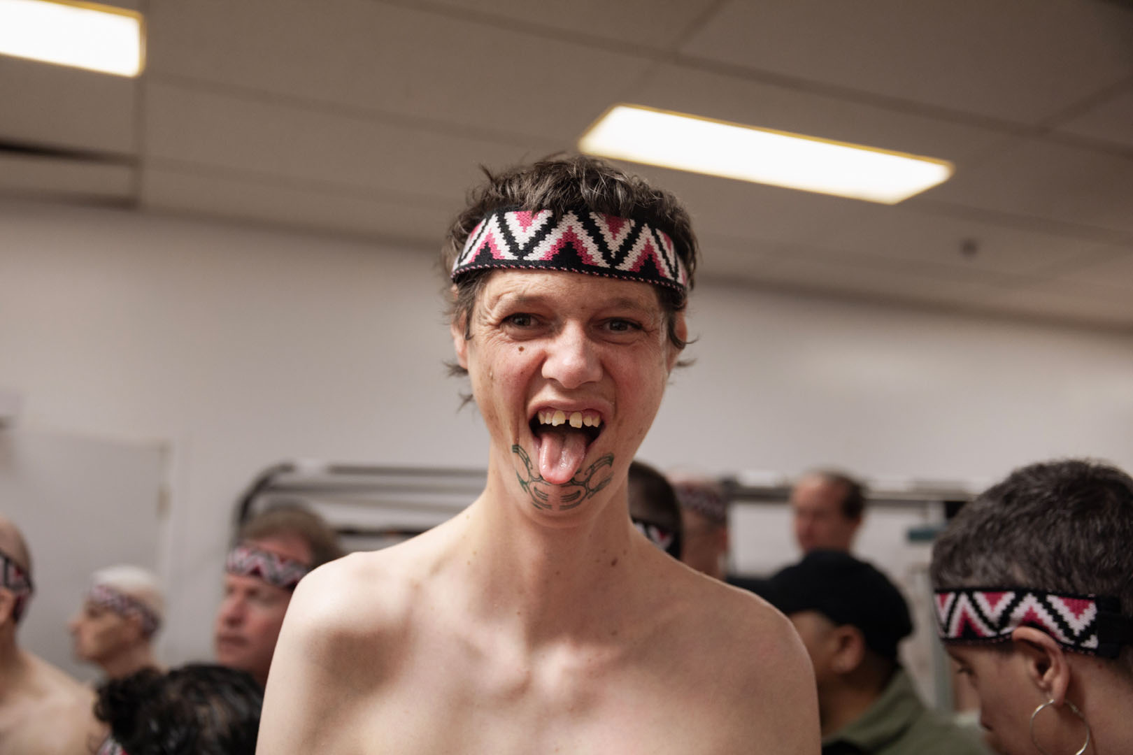 A kaihaka wearing a tīpare with ta moko on his chin does a pukana.