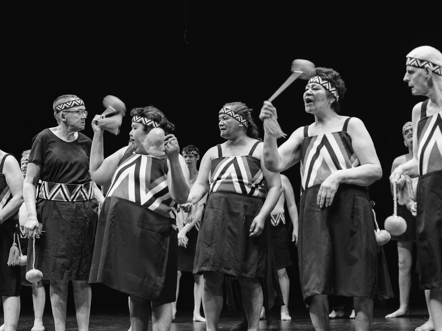 The kaihaka of Te Rōpu o te Hauāuru o Tāmaki perform on stage with poi. The photo is black and white. 