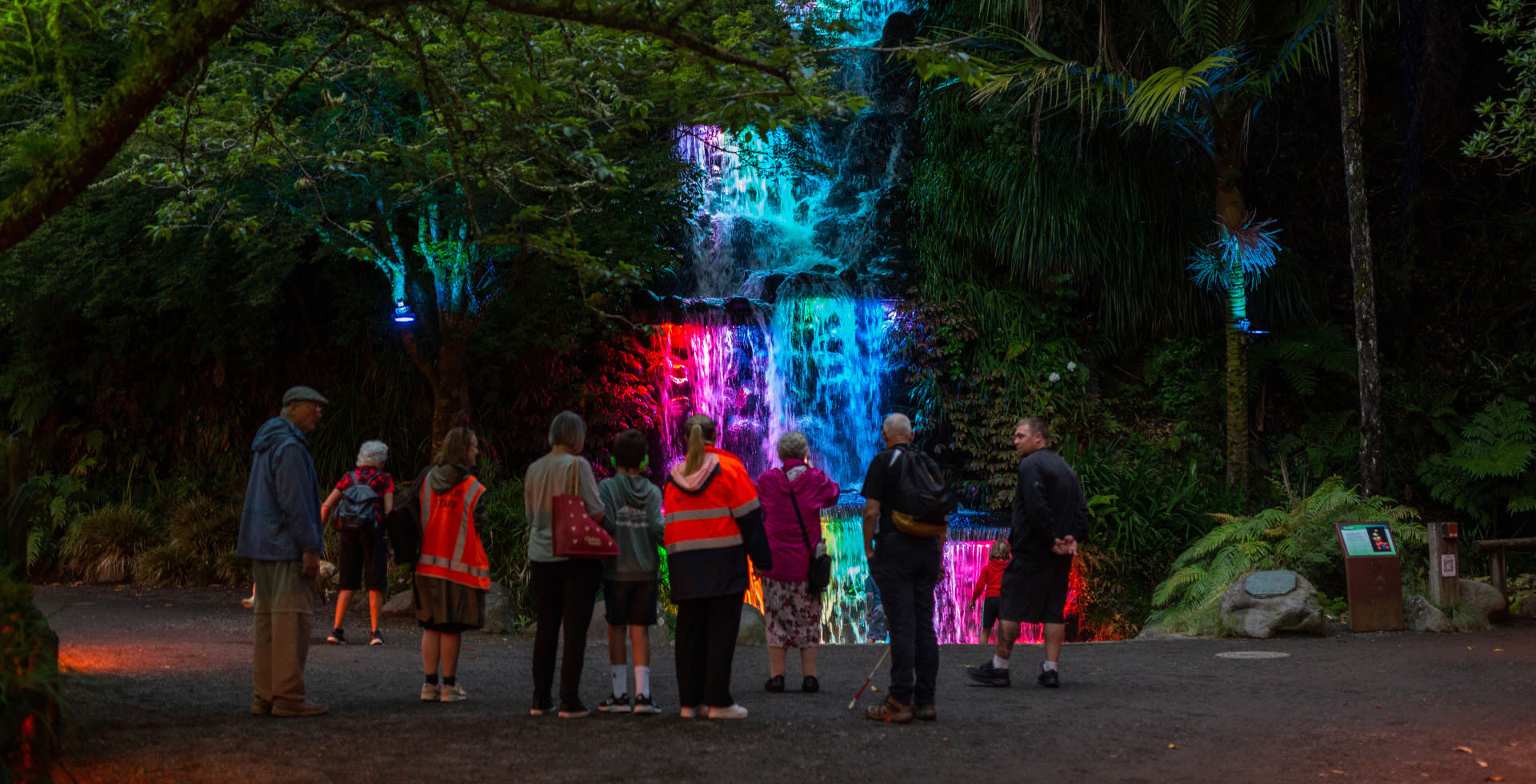 A waterfall is pink and blue lights coming out from it. There are people enjoying the view.