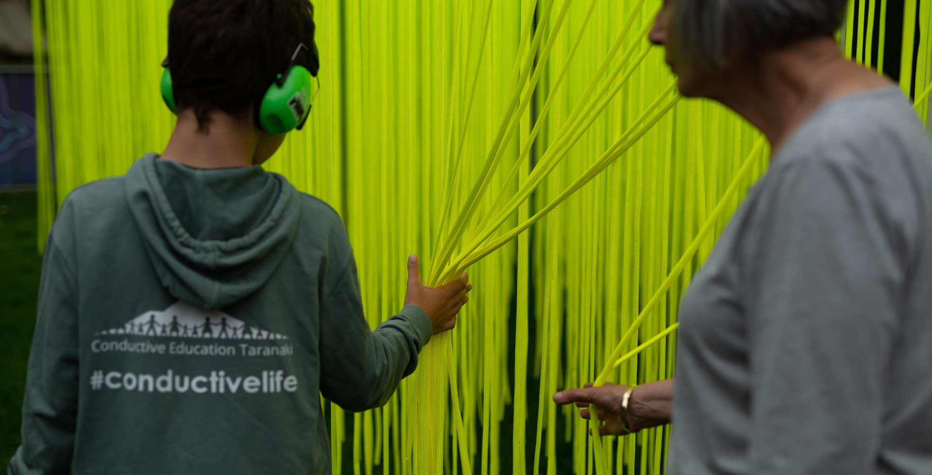 A young person wearing noise-cancelling headphones is touching a bunch of bright green rope.
