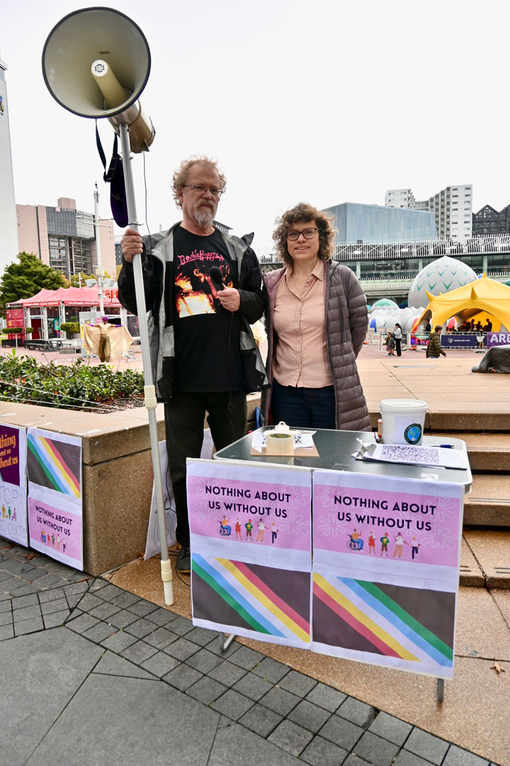 A man and woman hold a megaphone and stand in front of signs that read: Nothing about us without us.