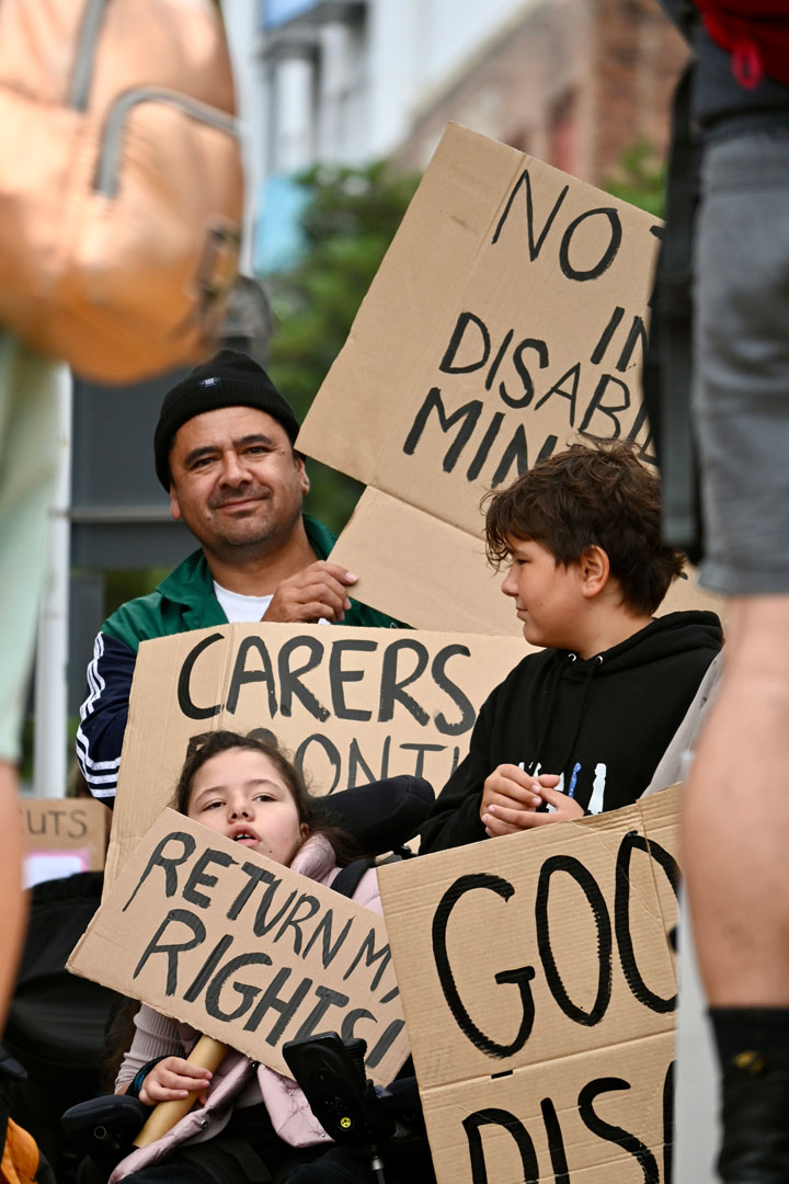 A dad and two kids hold up cardboard placards; one reads: Return my rights! 
