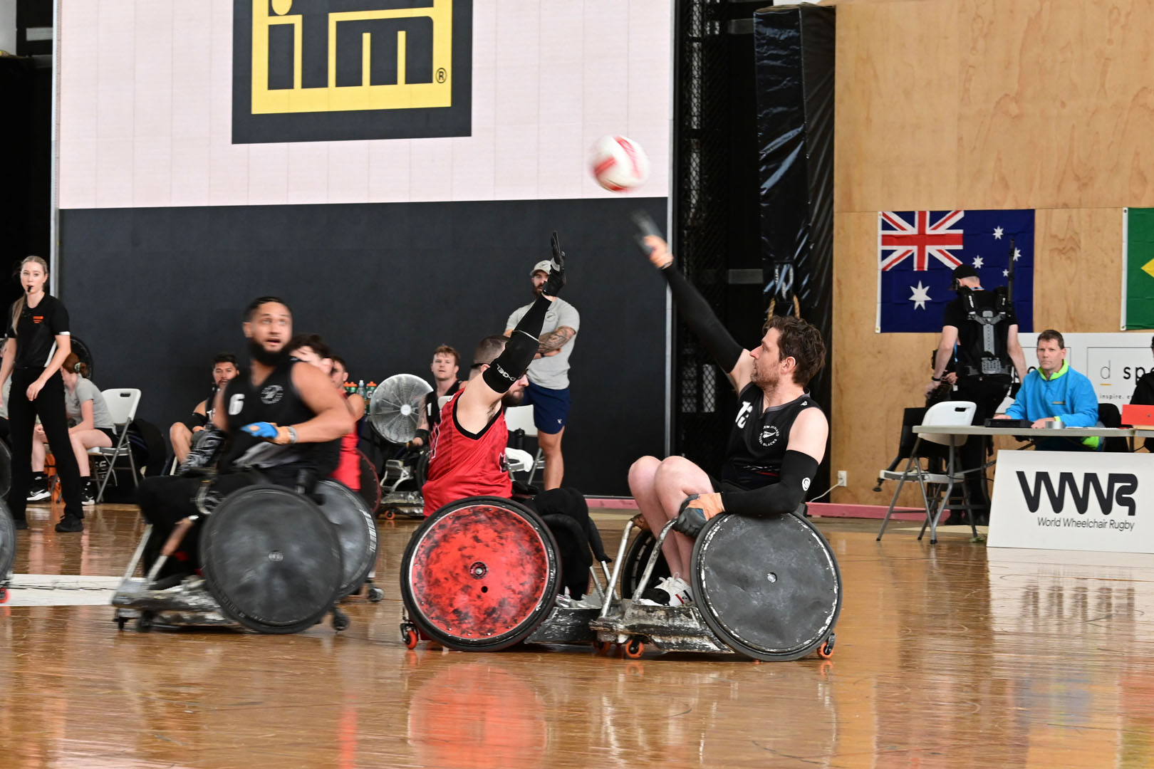 A Wheel Blacks athletes throws a ball high over a Canadian player on a wooden court.