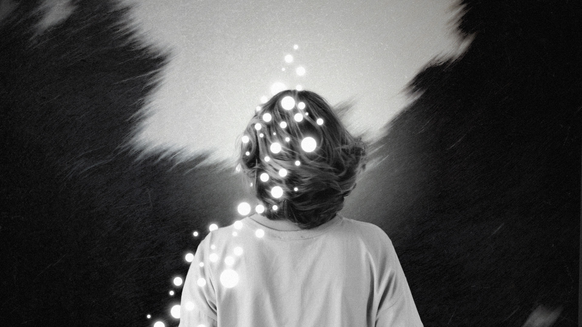 The back of an adolescent looking through a break of black figures, with lights coming from their back.