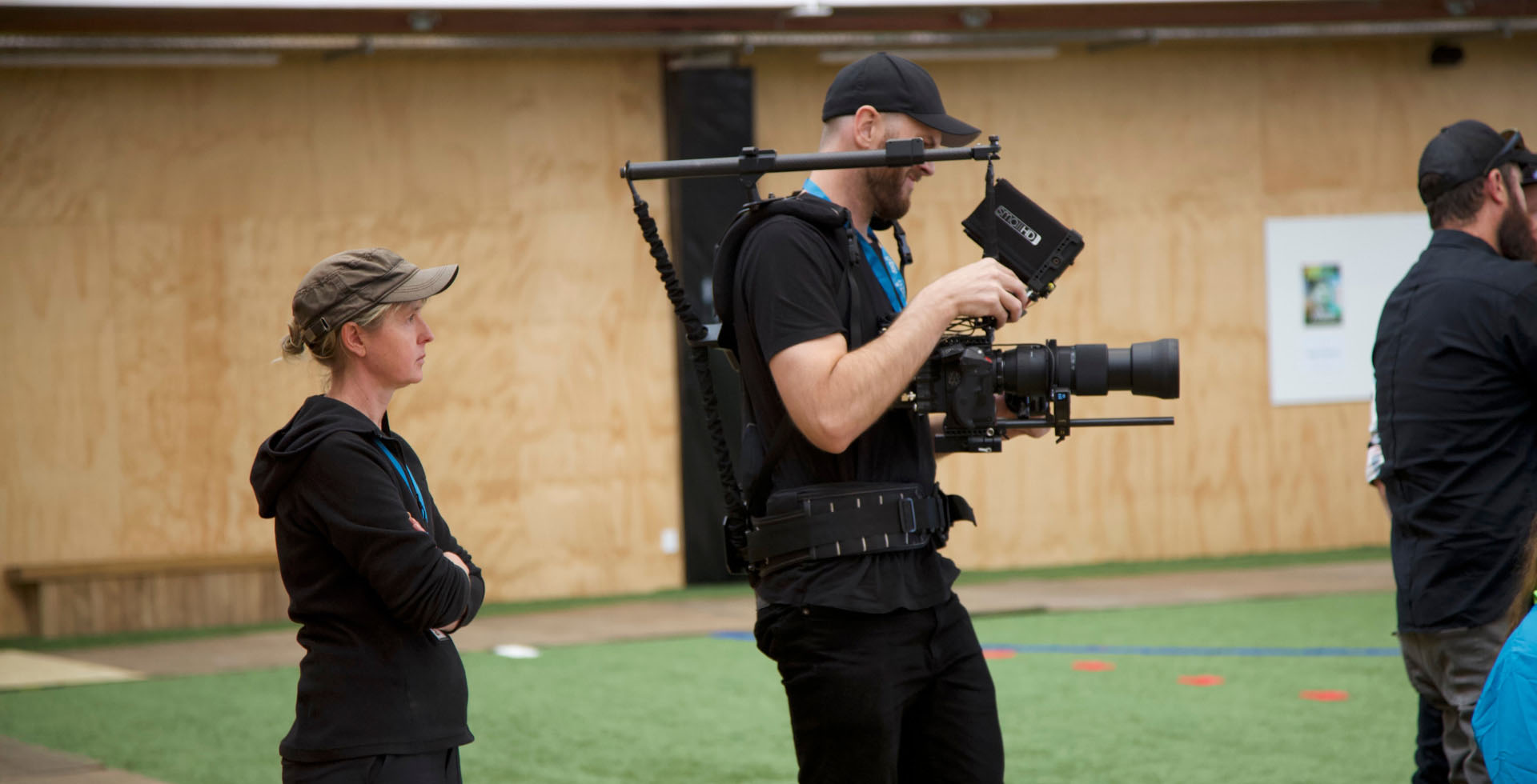 Robyn stands behind a camera operator in a sports gym.