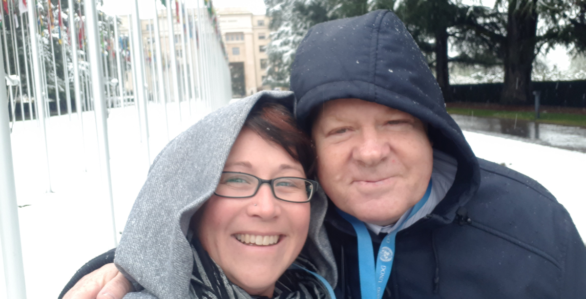 Alexia and Robert pictured outside in the snow outside at the UN; they are wearing hooded jackets and smile together at the camera.