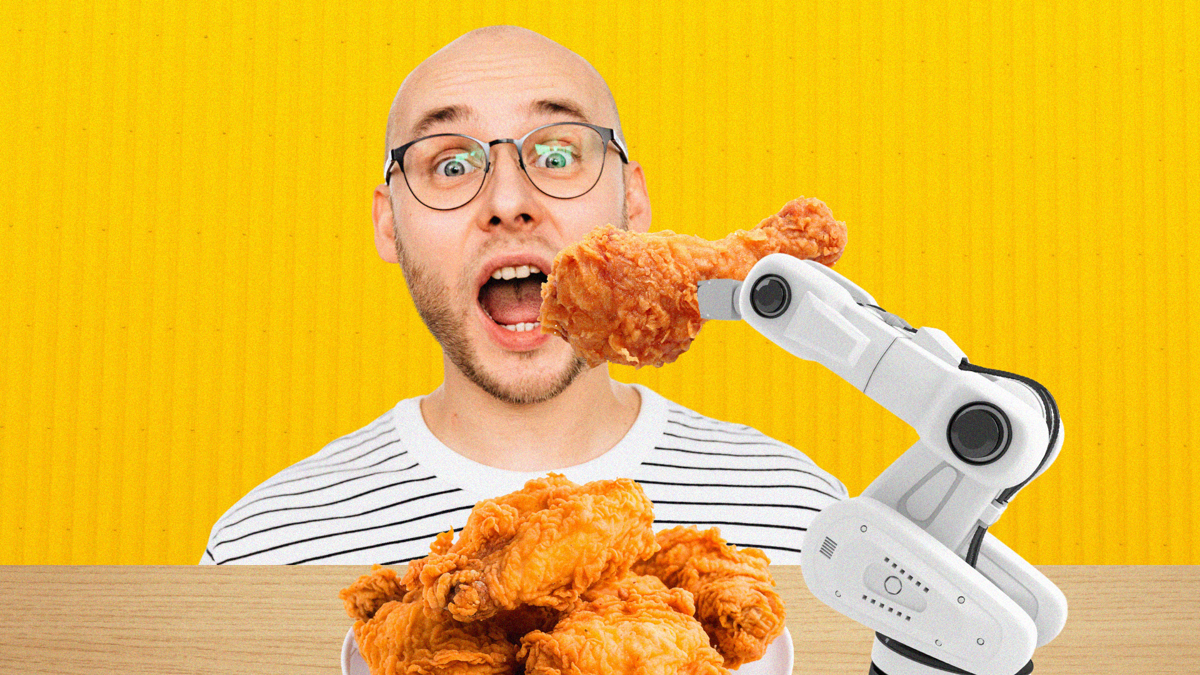 A white, bald man with glasses is excited to eat fried chicken and is being fed by a robotic arm.