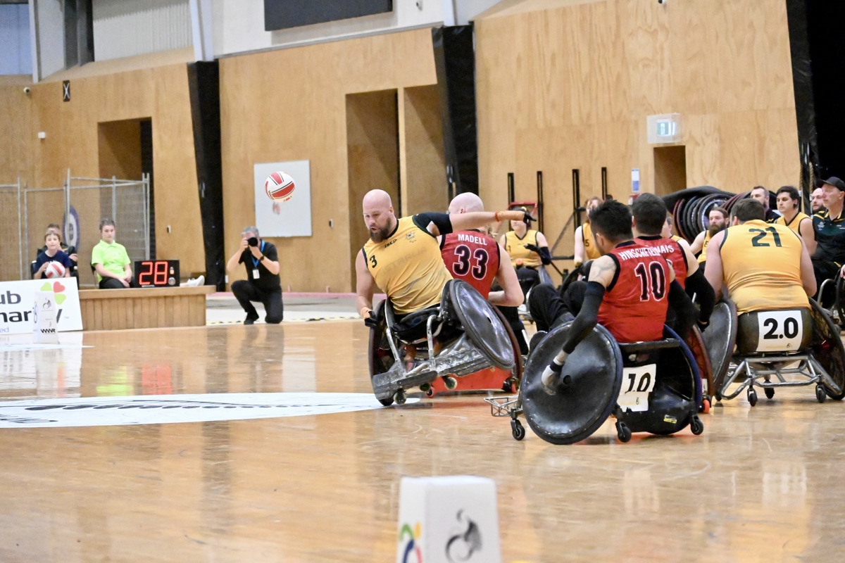 An Australian wheelchair rugby player tips in his chair on one wheel as other players crowd around him.