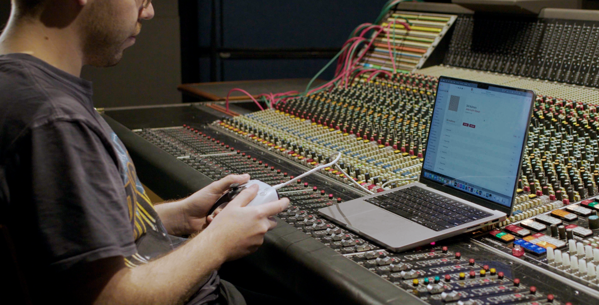 Jesse holds a PlayStation controller that is linked up to a laptop.