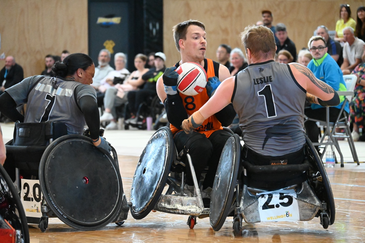 A wheelchair rugby athlete grabs the ball with his wheelchair leaning on one wheel and rams into another player.