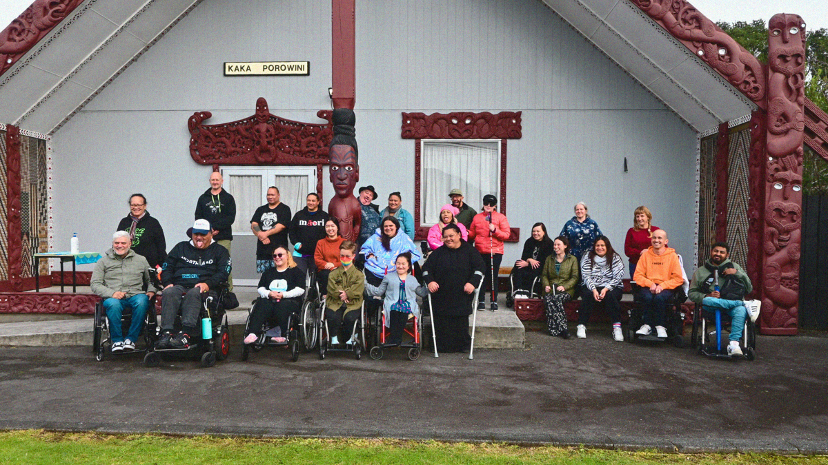 A group of 24 whānau hauā gather outside Terenga Paraoa Marae in Whangārei.