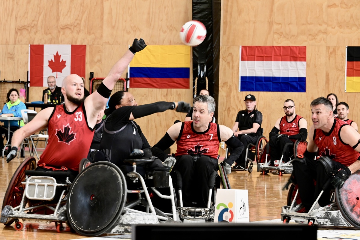 Players in a Canadian wheelchair rugby team are reaching for a ball from a New Zealand athlete.