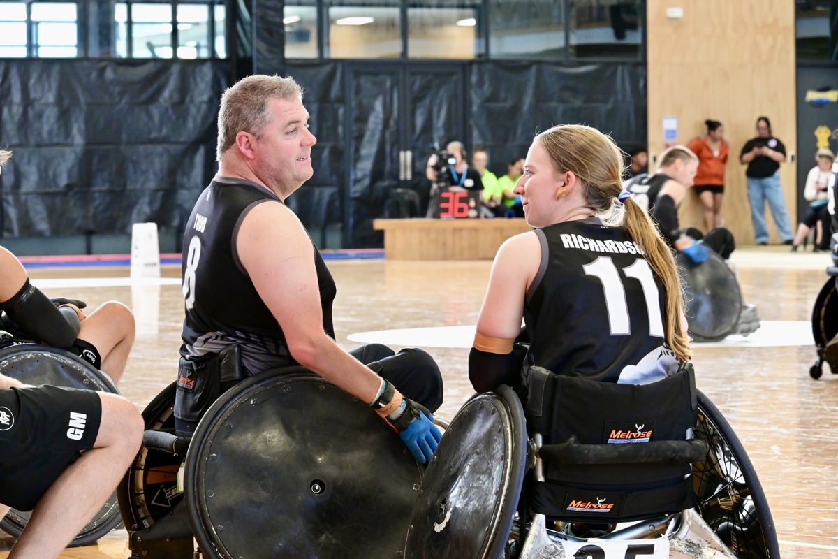 Mike Todd and Jacinta Richardson both sit in wheelchair rugby chairs and talk at the court side. 