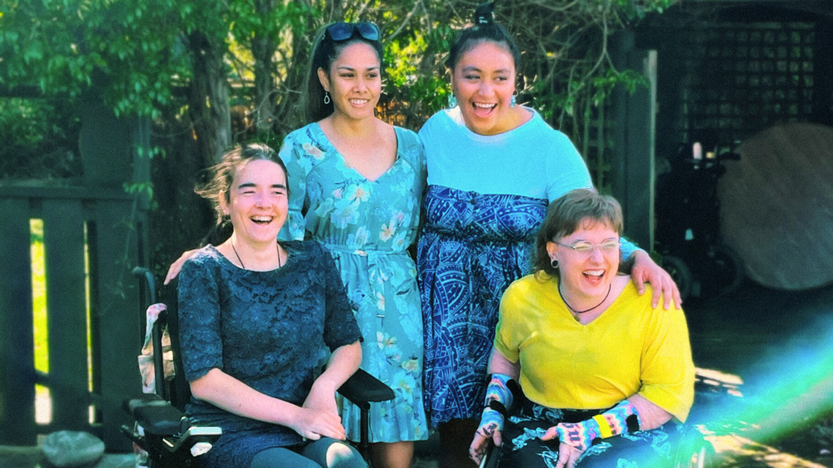 Four young people wear bright clothes and laugh; two of them use wheelchairs. 