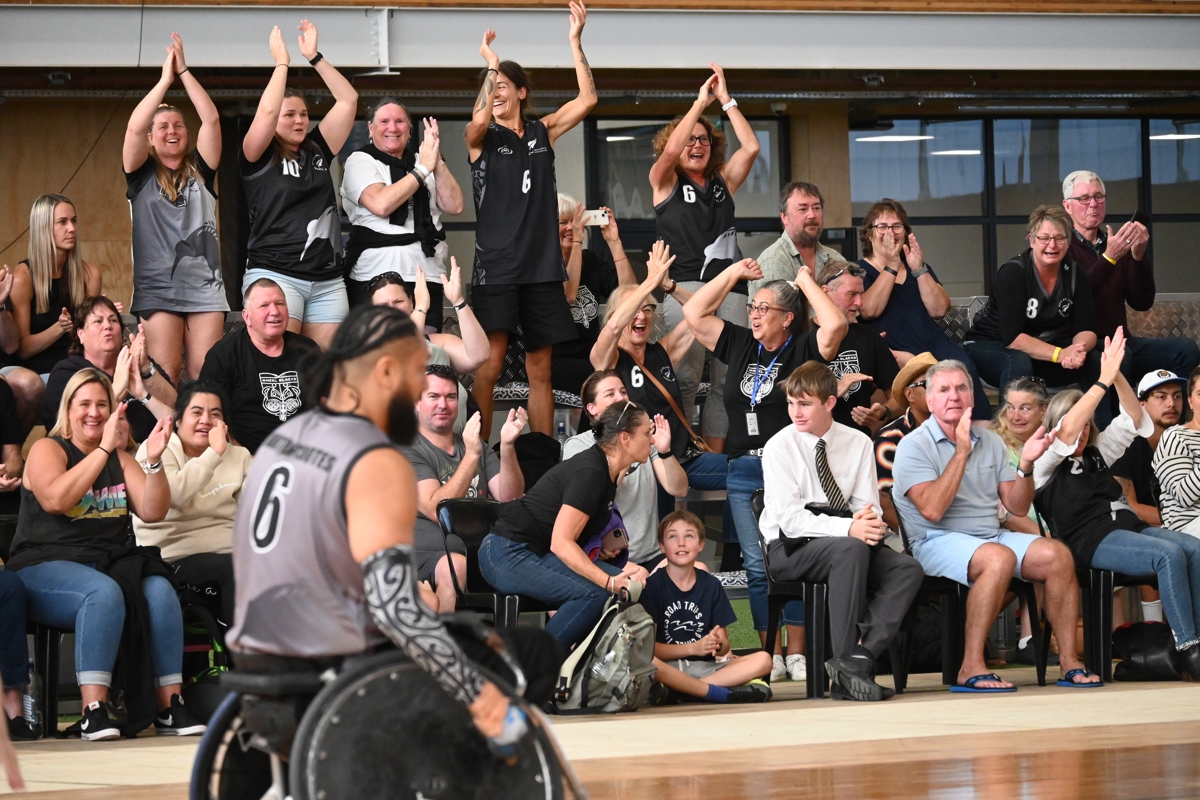Team New Zealand supporters clap and smile from the sidelines.