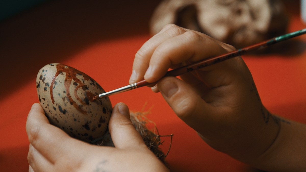 A close-up of Ruby's hands painting an egg with brown paint.