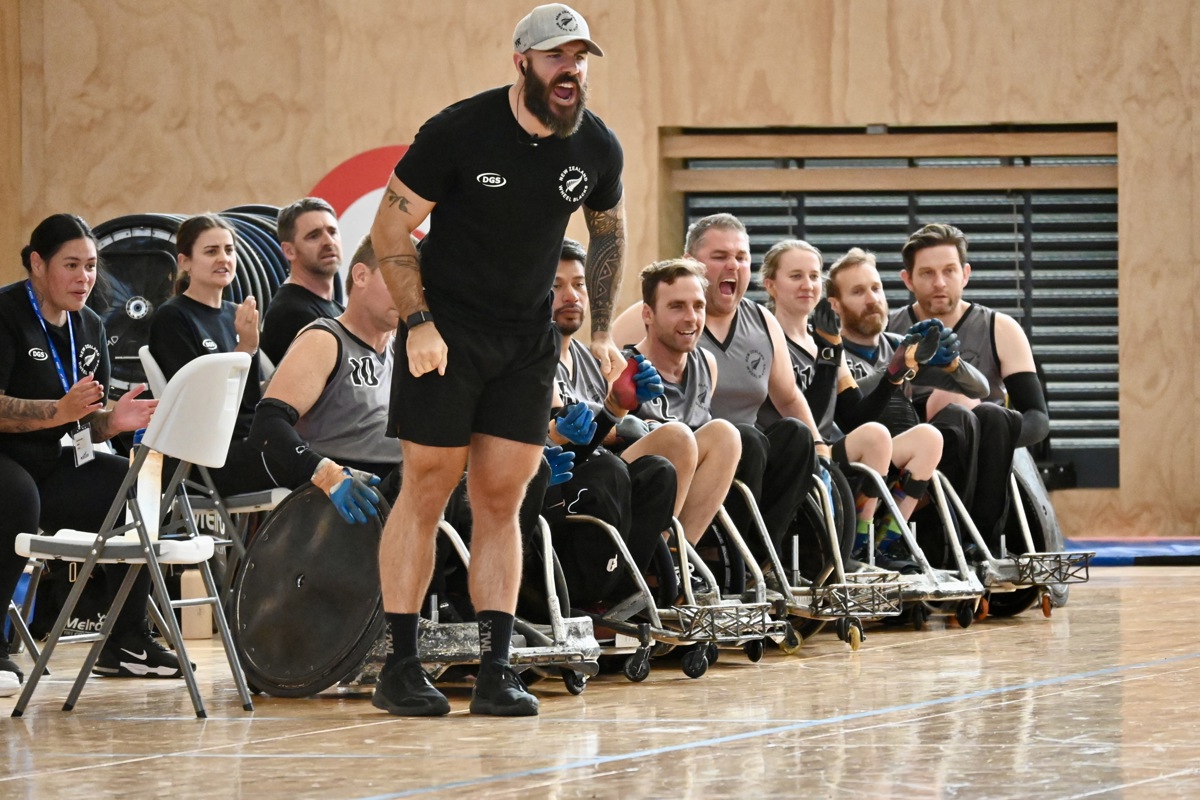 A coach of the Wheel Blacks stands and yells passionately; the rest of the team line up behind him also looking excited.