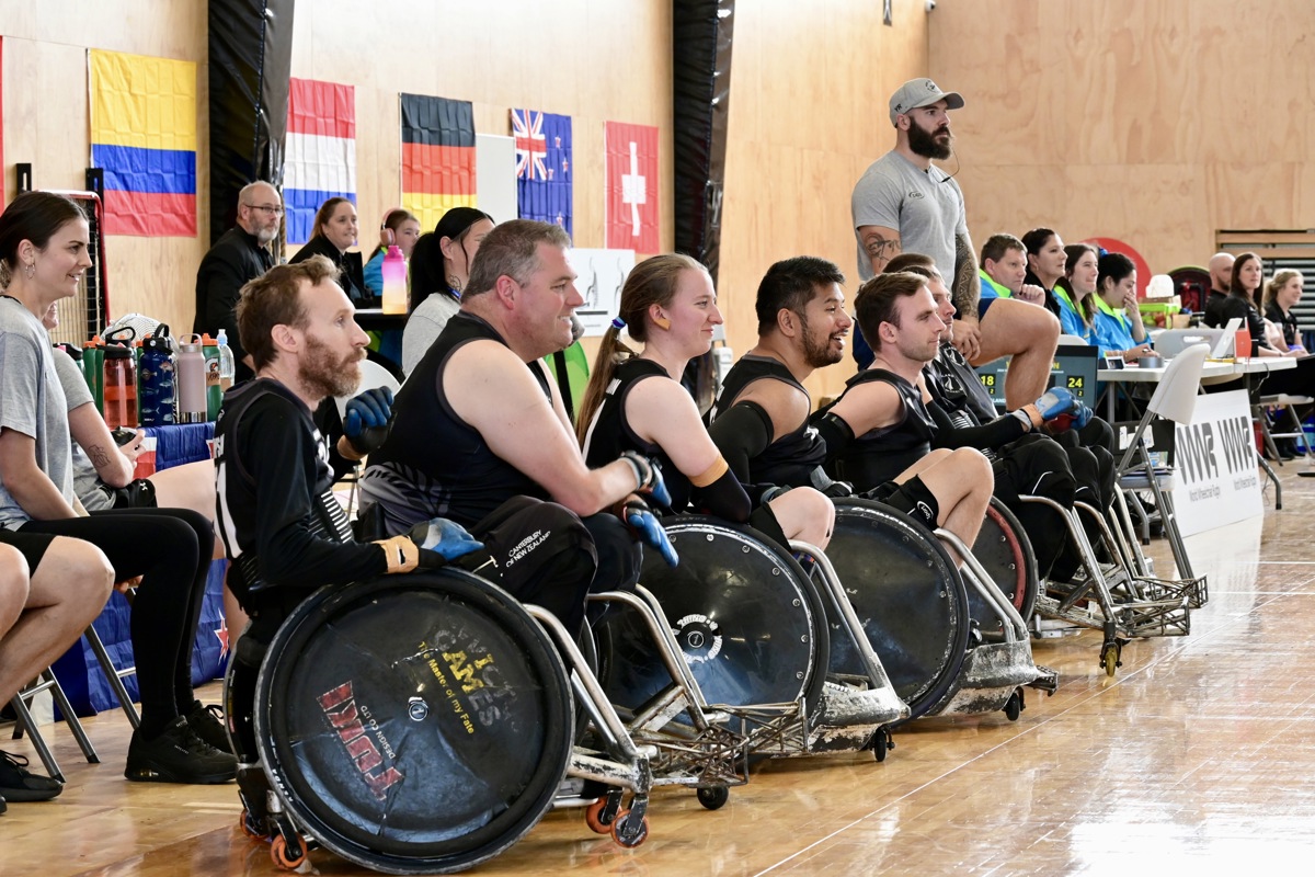Six Wheel Blacks athletes are lined up on a court side and engaged watching the sport.