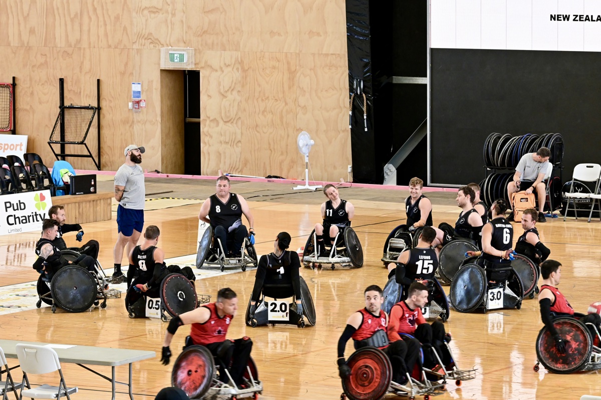 A team of 12 Wheel Blacks athletes are in a circle on a court doing stretches and warm ups. 