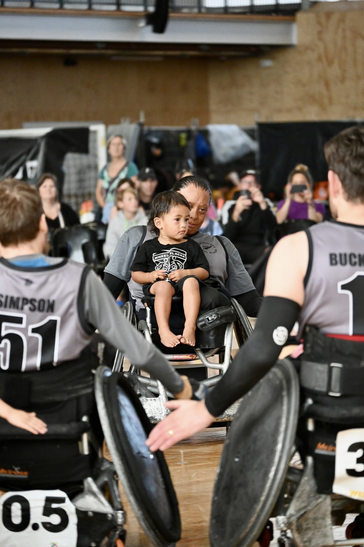A small child sits on the lap of a wheelchair rugby athlete.