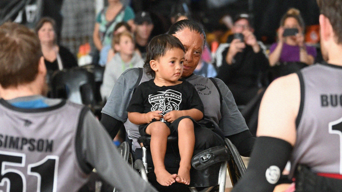 A small child sits on the lap of a wheelchair rugby athlete.