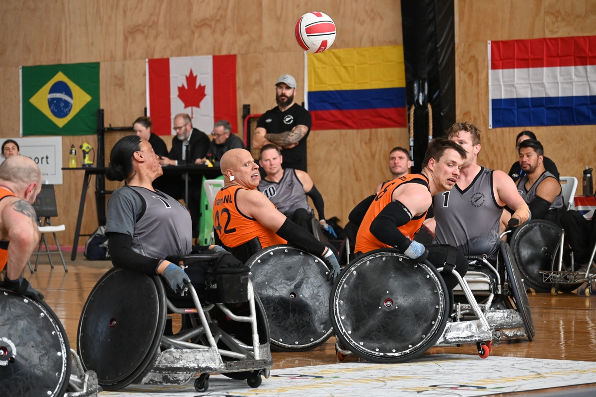 Wheelchair rugby athletes bash into each other in their chairs with the ball flying over their heads.